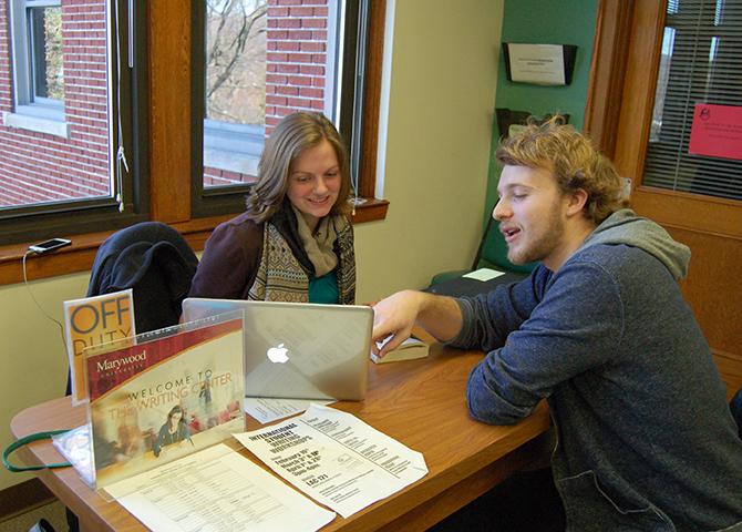 Tutors+Lindsey+Crean+and+Gavin+Coyle+chat+at+the+Writing+Center+Desk.